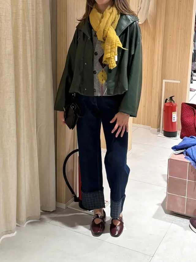Green leather jacket with a yellow scarf and dark jeans