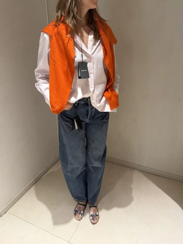 White shirt with an orange sweater over the shoulders and jeans